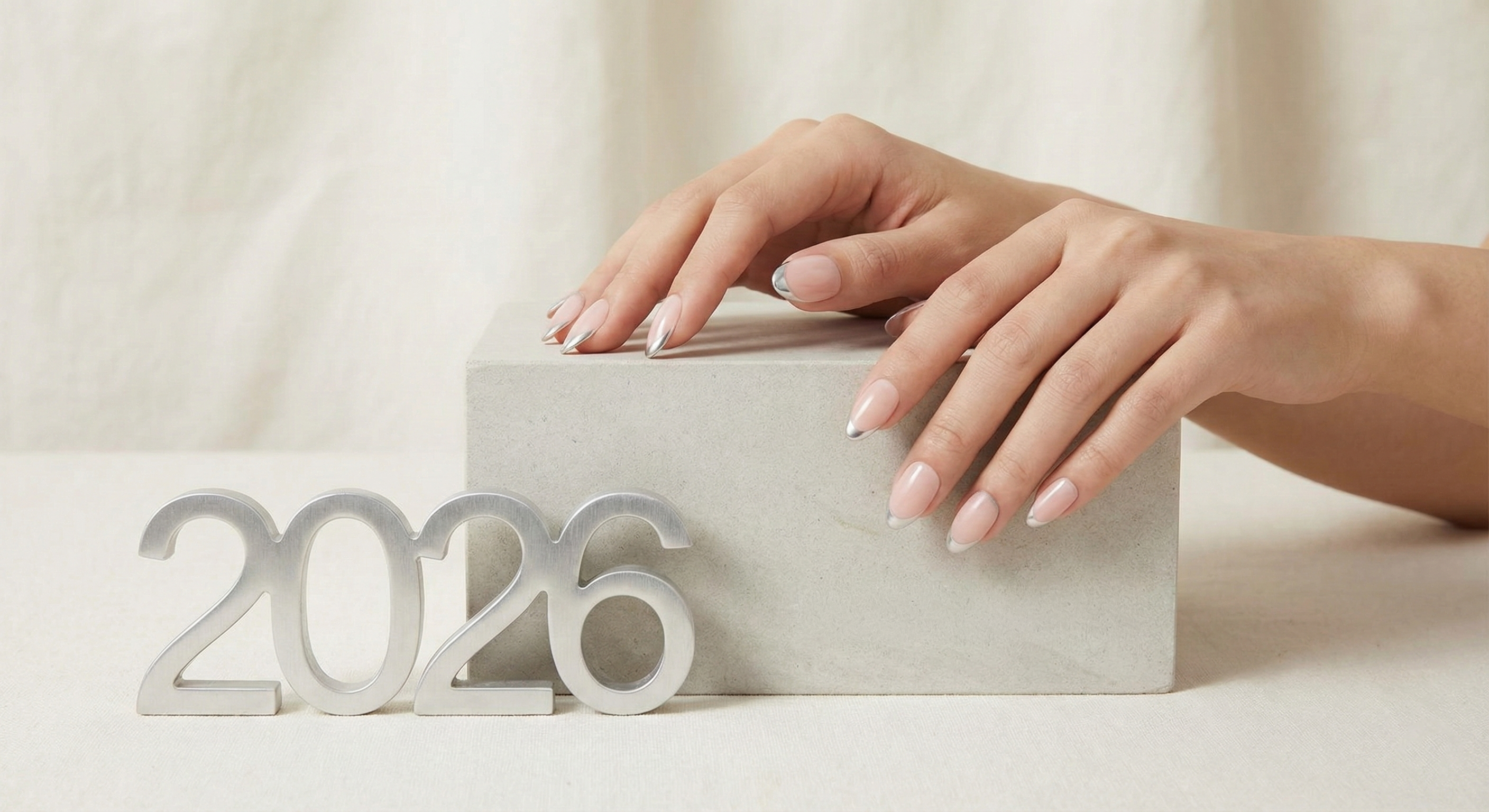 Woman's hands with silver-tipped press-on nails resting on block, 2026 silver numbers in front
