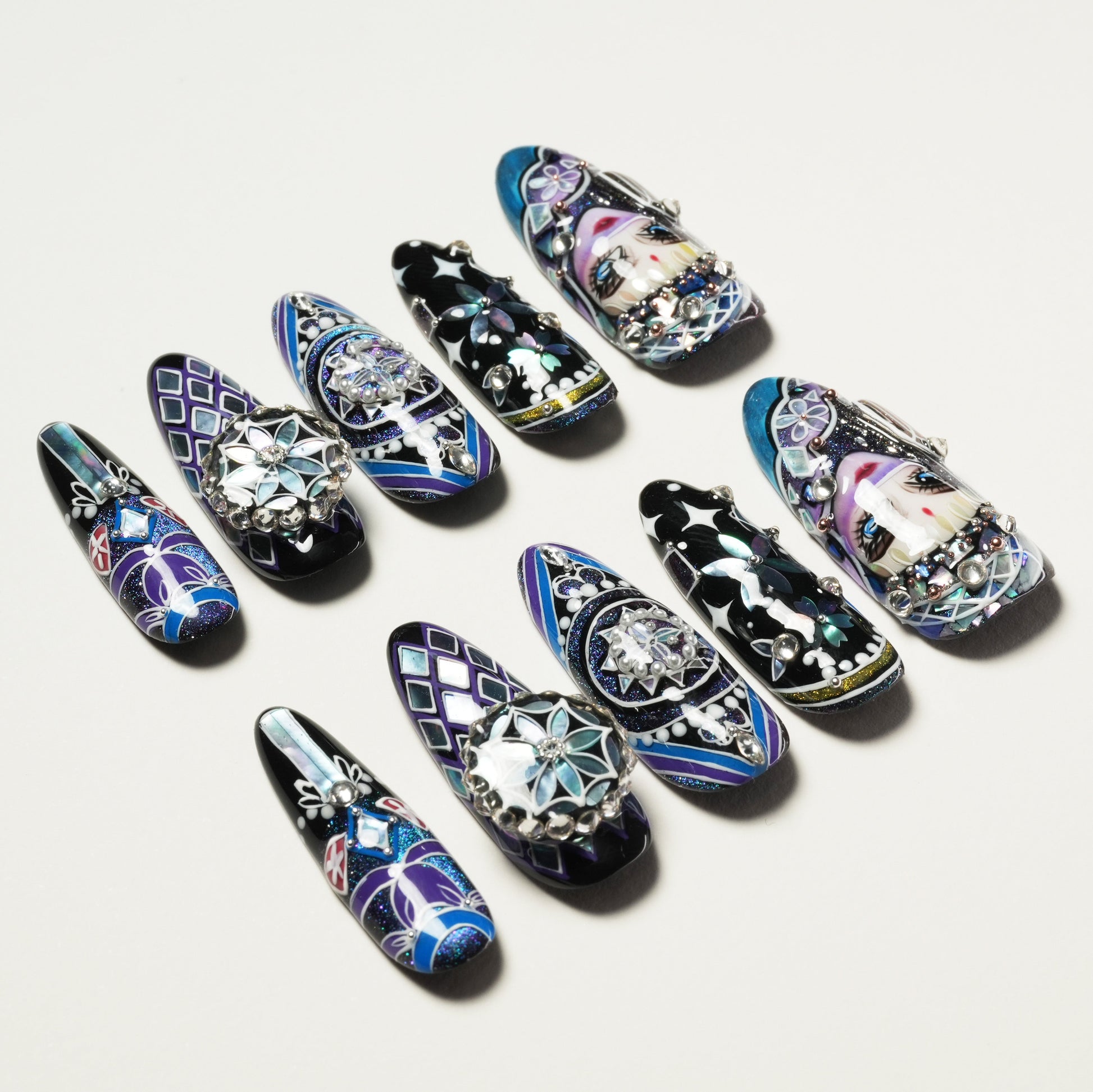 Set of long, ornate blue and black press-on nails with intricate floral and face designs