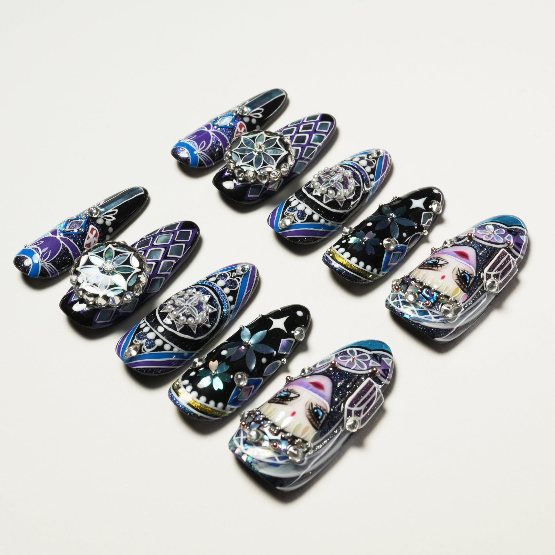 Set of detailed, hand-painted long false nails with floral, geometric, and face designs in blue, black, and purple