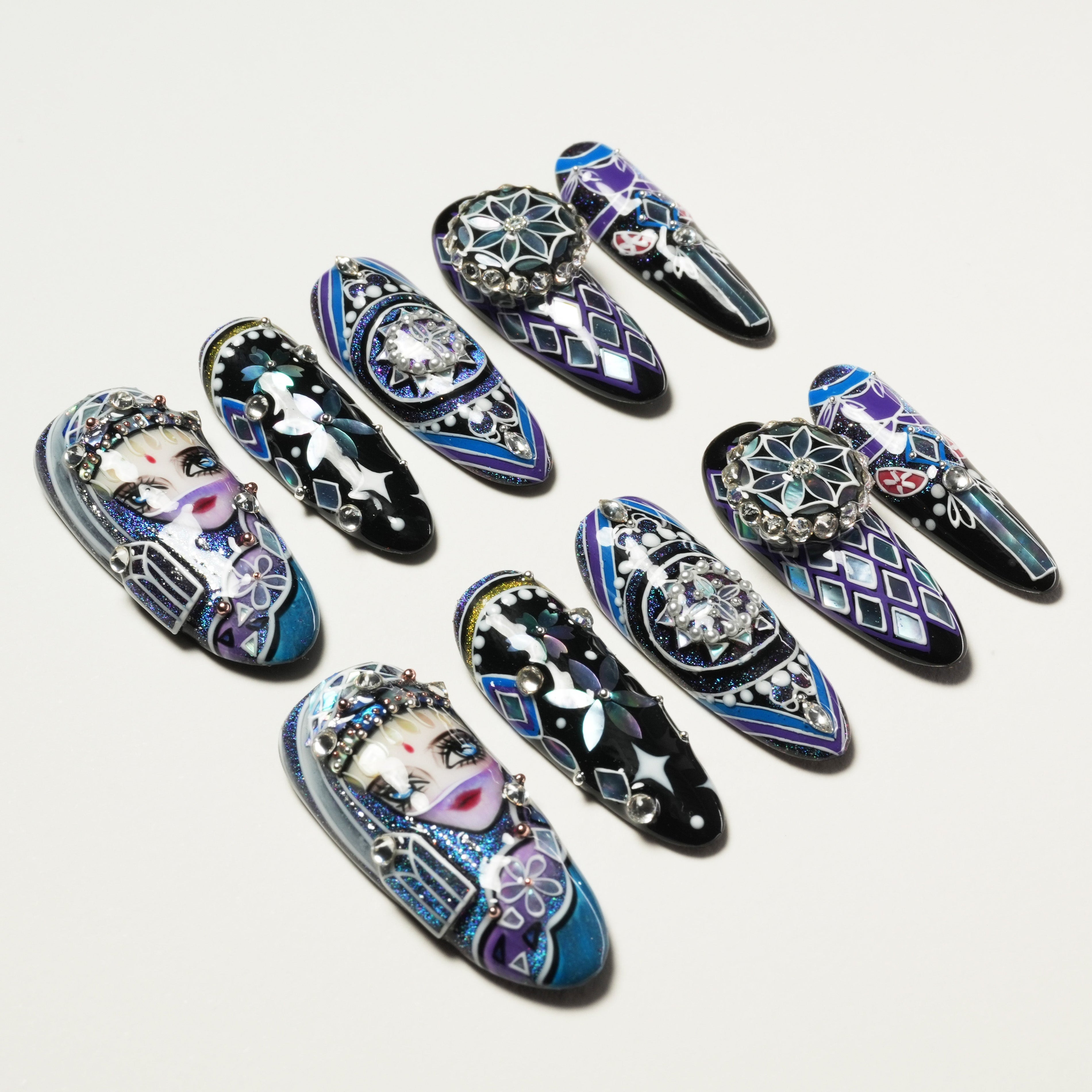 Set of long artificial nails with intricate purple, blue, and black designs, rhinestones, and painted faces