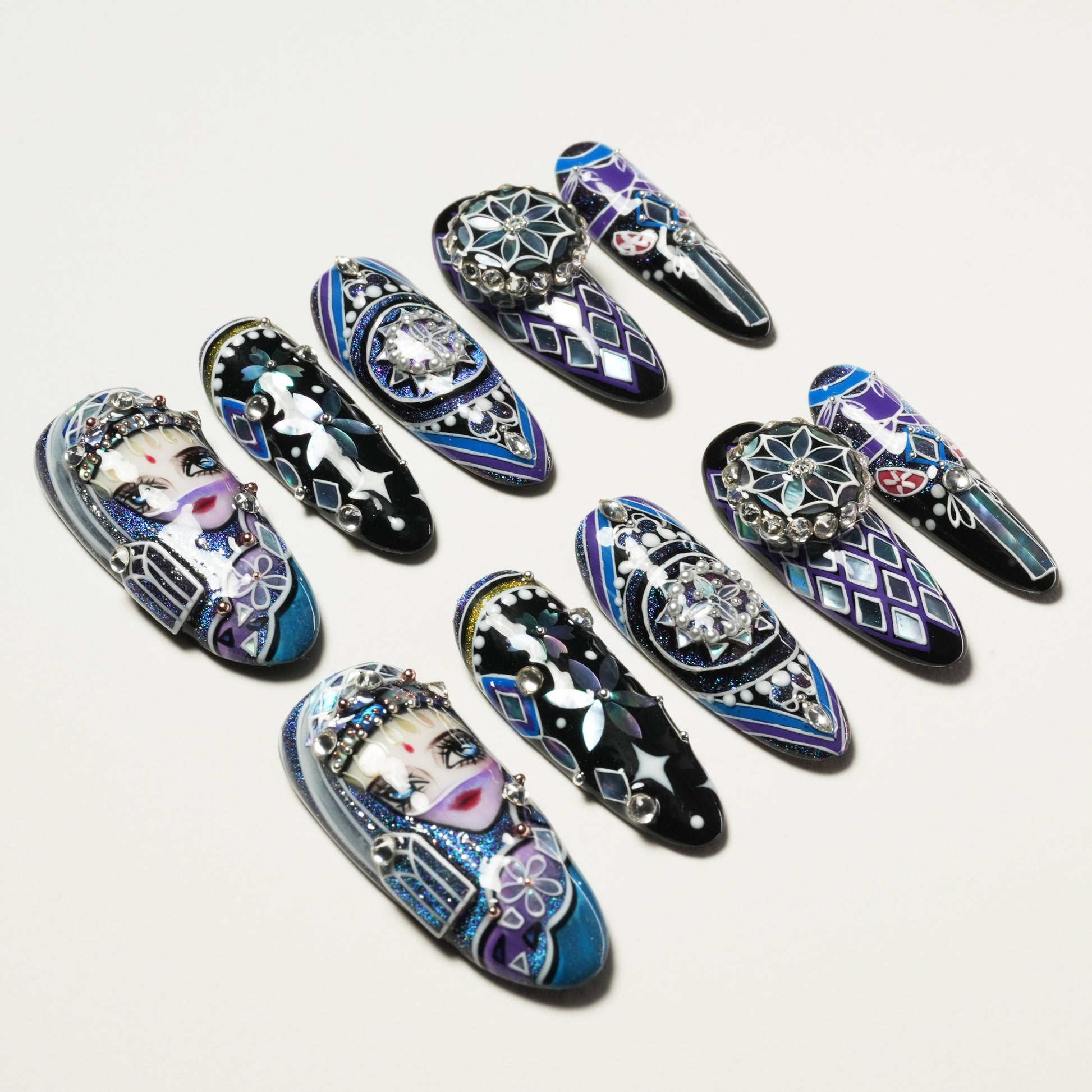 Set of long artificial nails with intricate purple, blue, and black designs, rhinestones, and painted faces