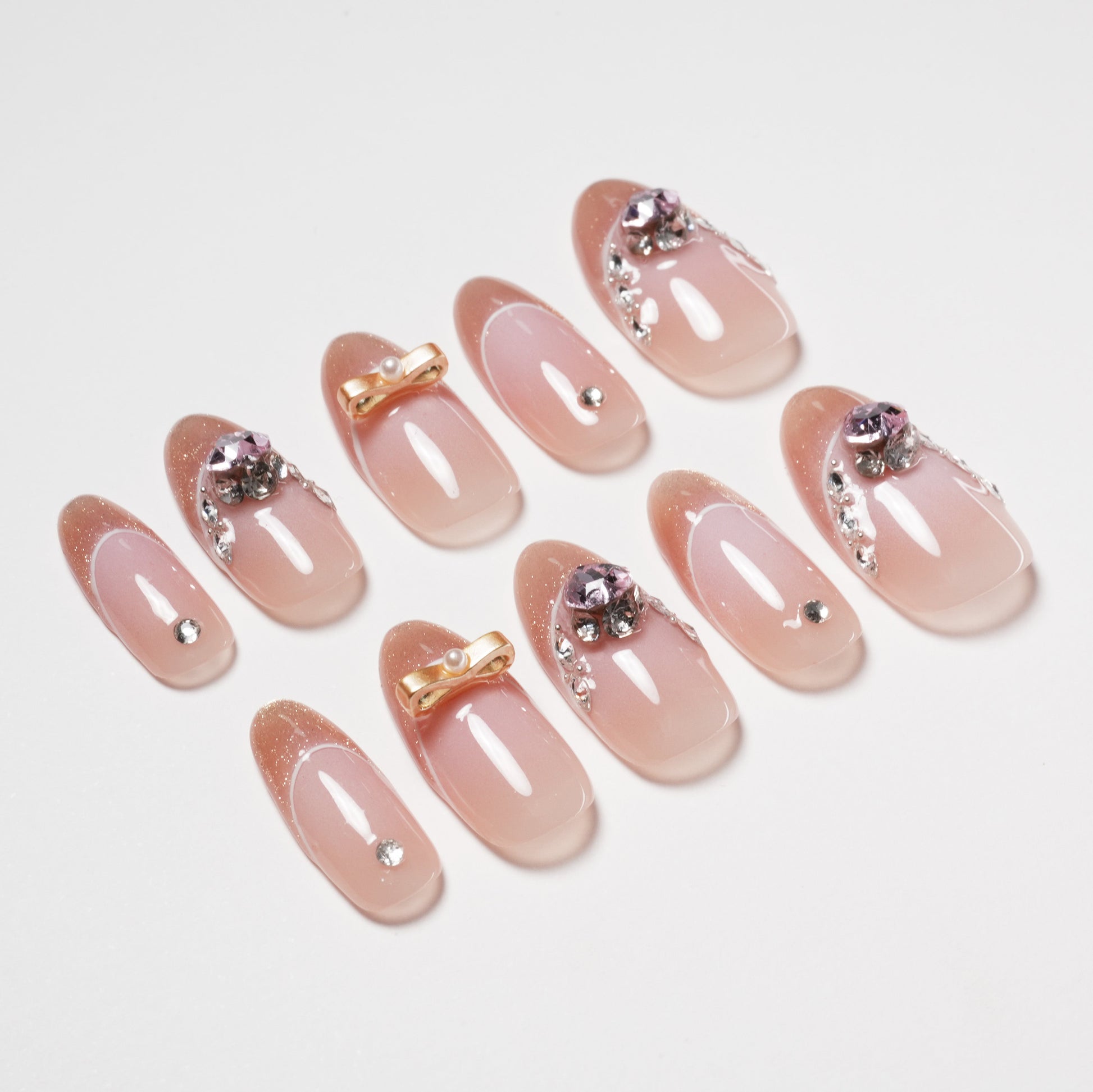 Handmade press-on nails with nude pink base, rhinestone and gold bow accents
