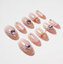 Handmade press-on nails in nude pink with heart-shaped gems, rhinestones, and gold accents