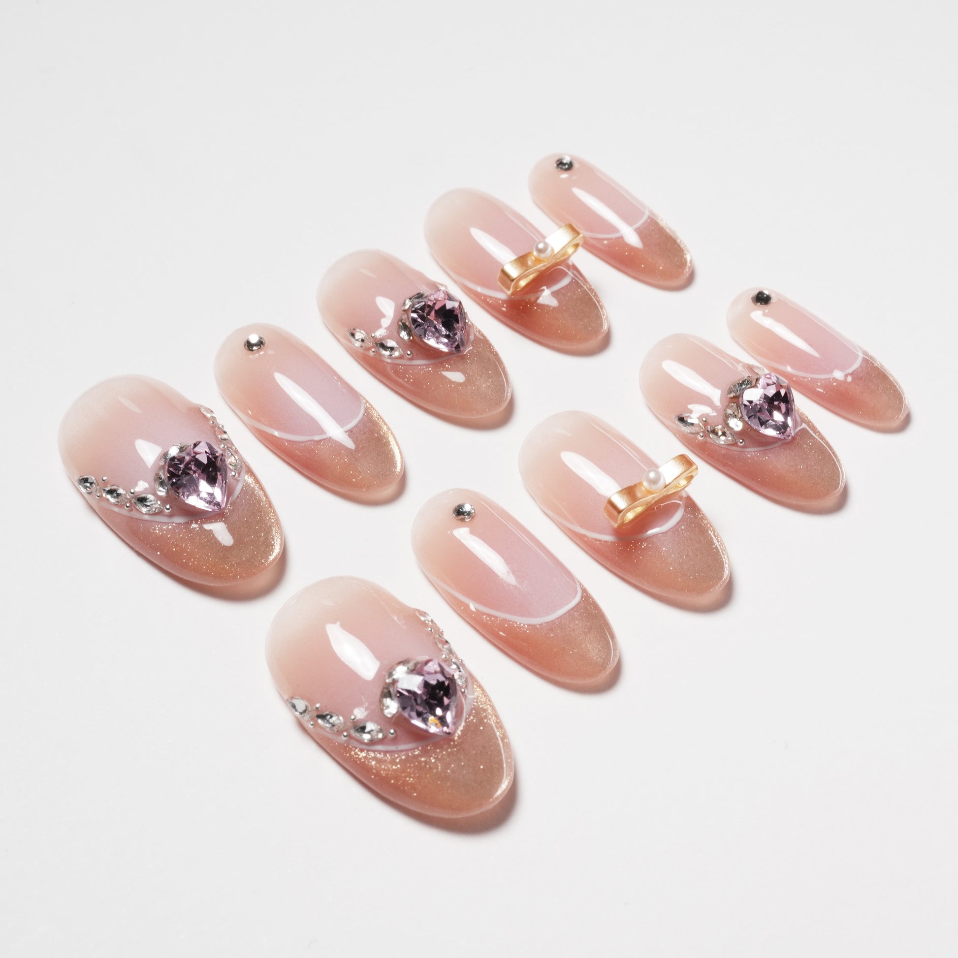 Handmade press-on nails in nude pink with heart-shaped gems, rhinestones, and gold accents