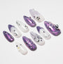 Handmade press-on nails with purple pearlescent designs, 3D gems, and abstract patterns