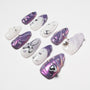 Purple and white press-on nails with butterfly, pearl, and gem accents, glossy finish