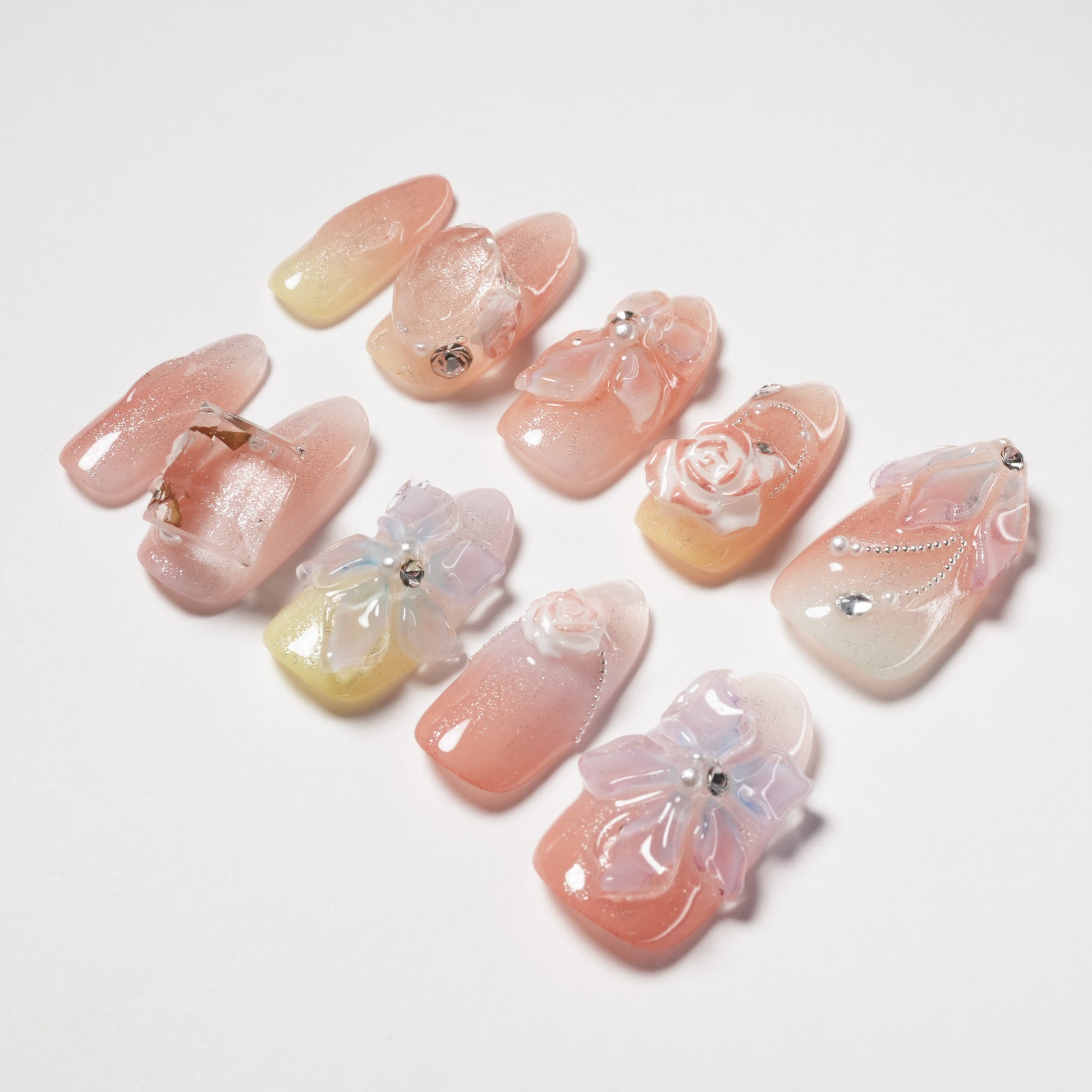 Handmade press-on nails with pastel ombre, 3D flowers, gems, and glitter accents on white background