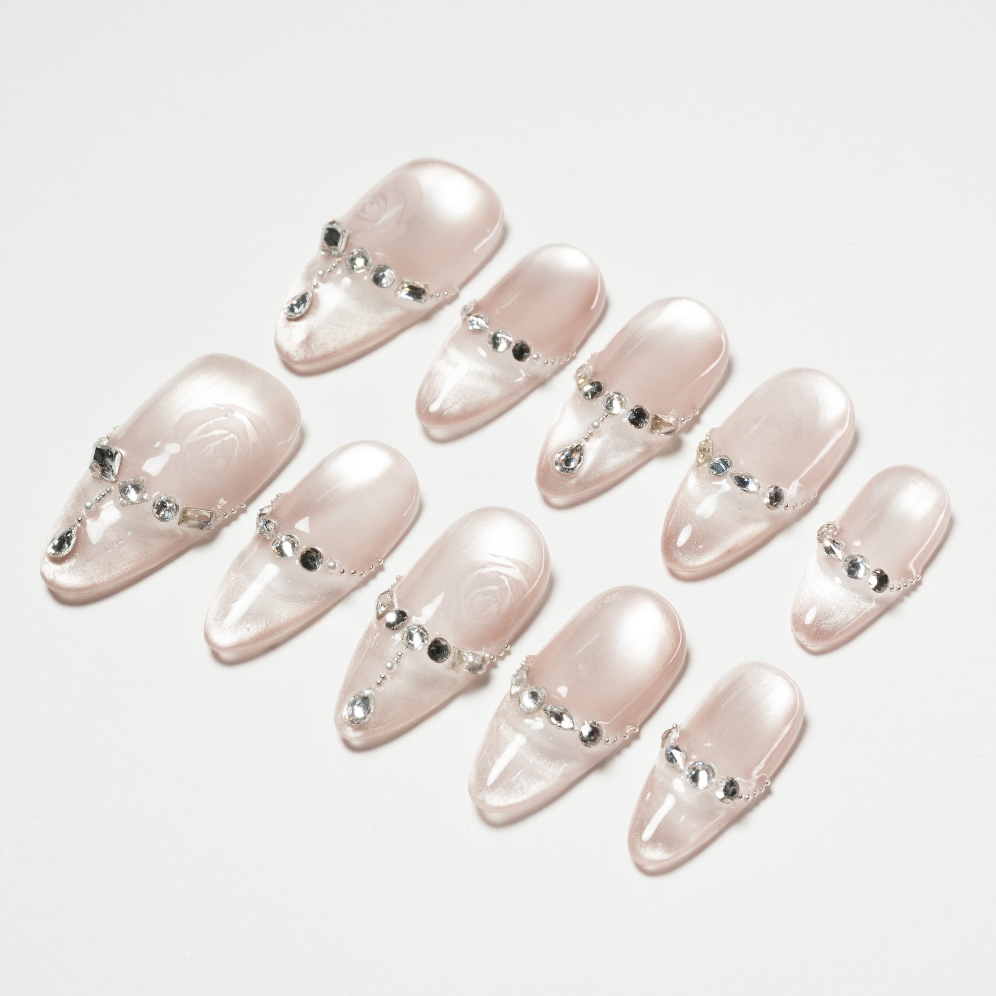 Set of glossy light pink false nails with rhinestone and pearl embellishments on white background