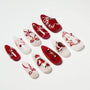 Red and white press-on nails with heart and bow designs, pearls, and rhinestone accents