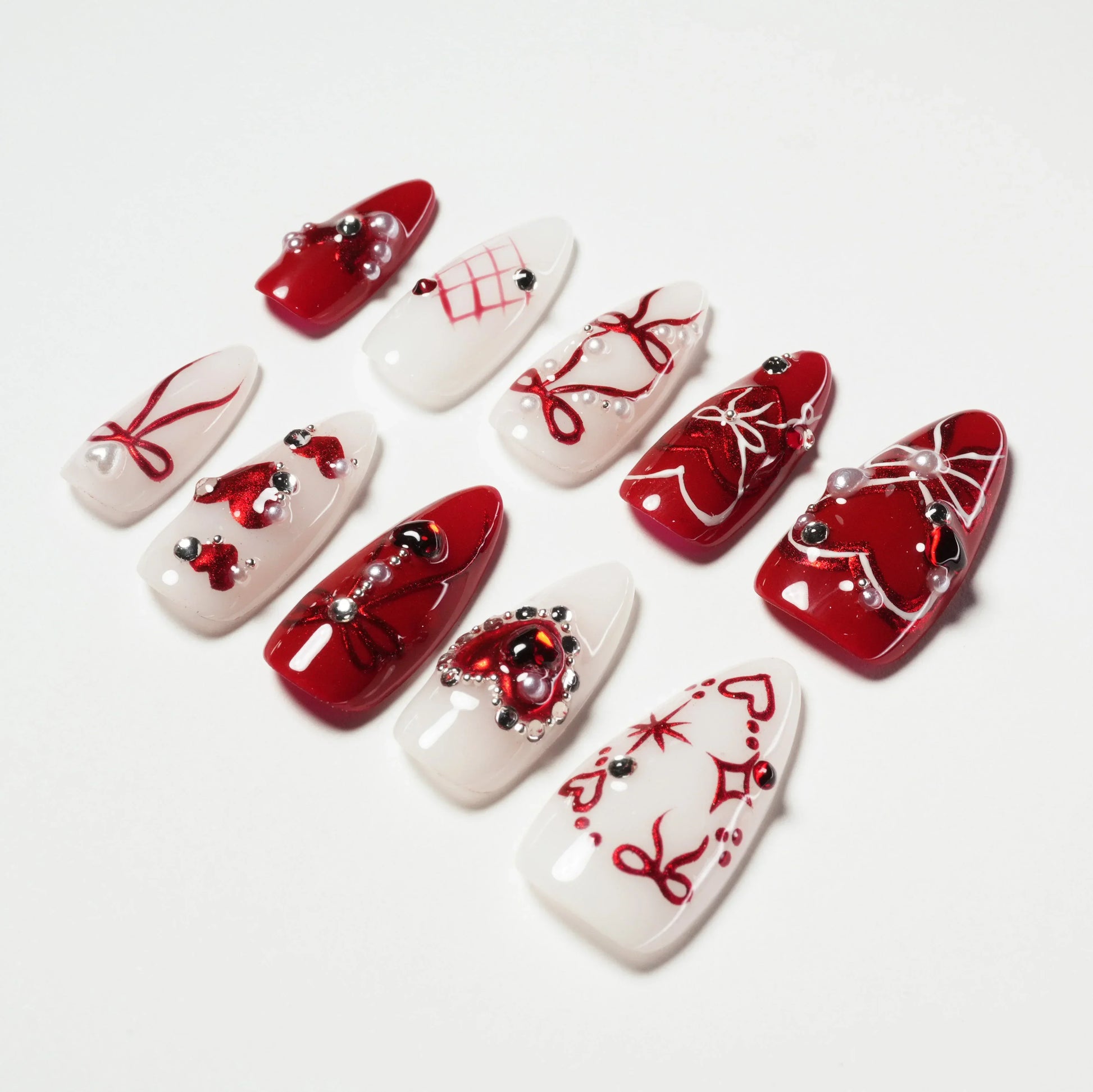 Red and white press-on nails with heart designs, pearls, and intricate nail art accents