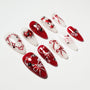 Red and white handmade press-on nails with heart, bow, and pearl designs on a white background.