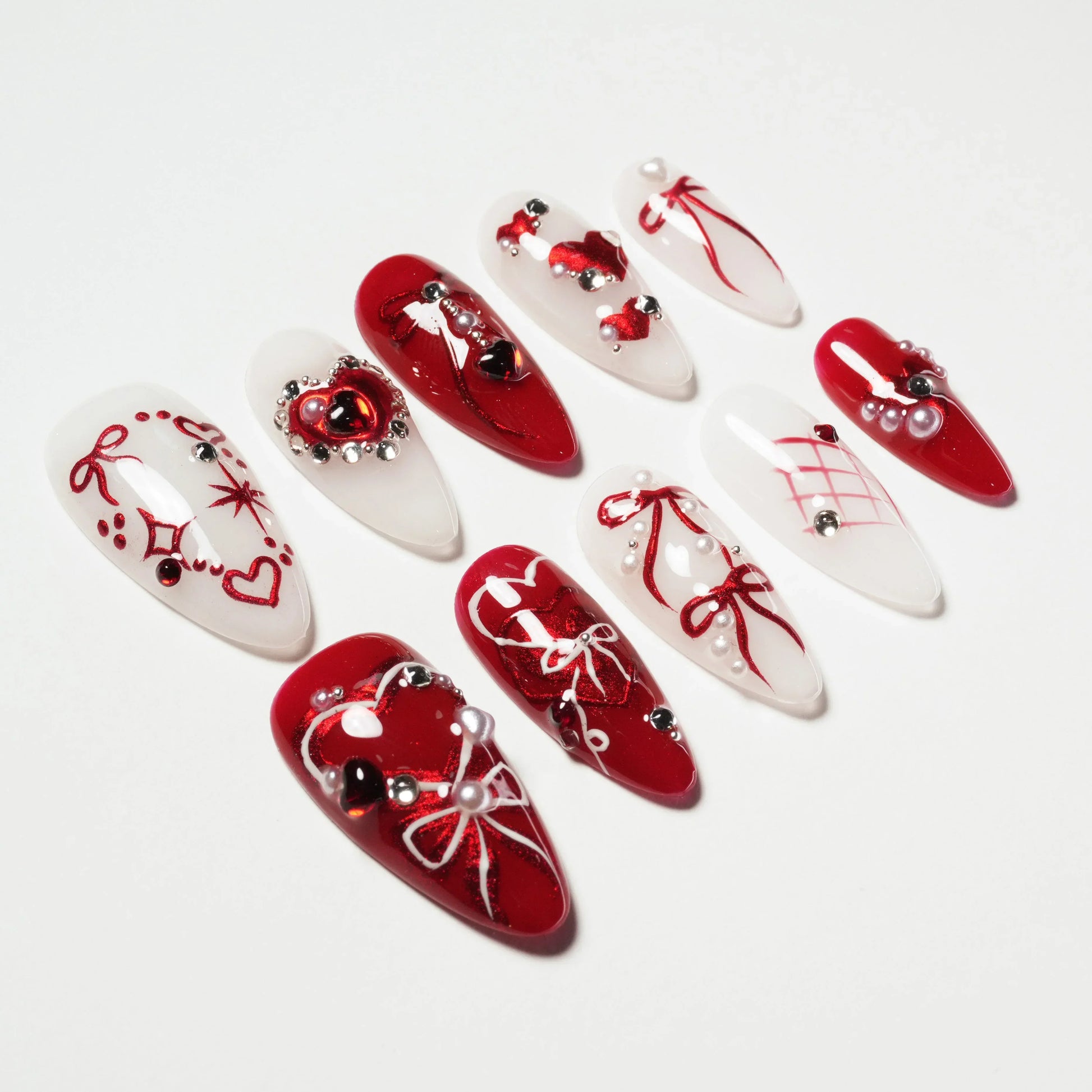 Red and white handmade press-on nails with heart, bow, and pearl designs on a white background.