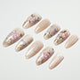 Handmade press-on nails with nude shimmer base and pink floral design, arranged on white background