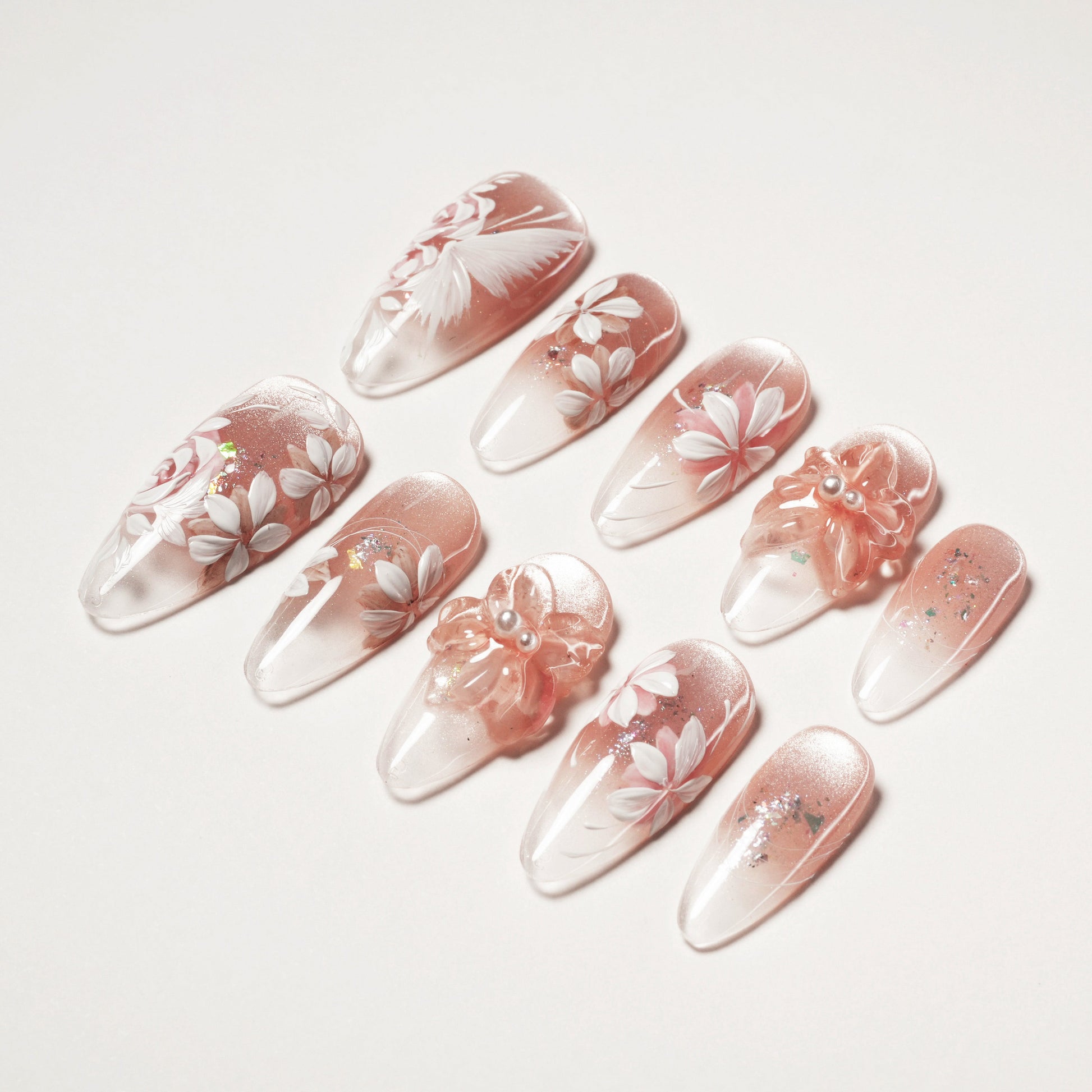Handmade press-on nails with pink gradient, white floral designs, 3D flowers, and glitter accents