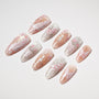 Handmade press-on nails with floral and feather designs in pink, white, and glitter accents