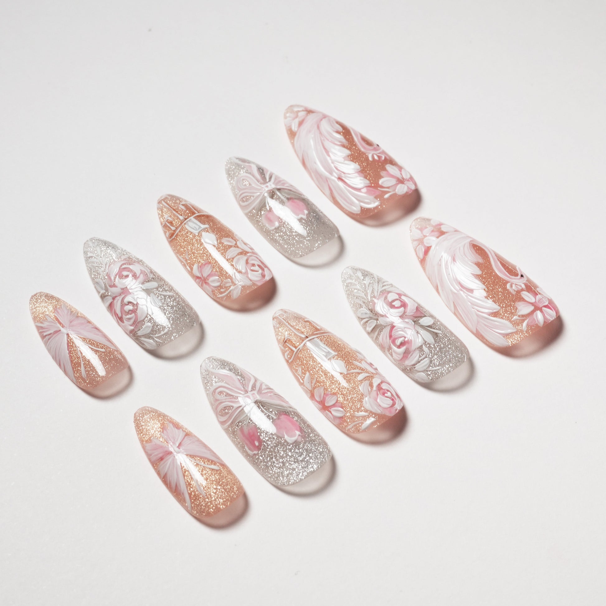 Handmade press-on nails with pink, white, and glitter floral designs on a white background