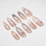 Handmade press-on nails with nude base and white floral designs, stiletto shape