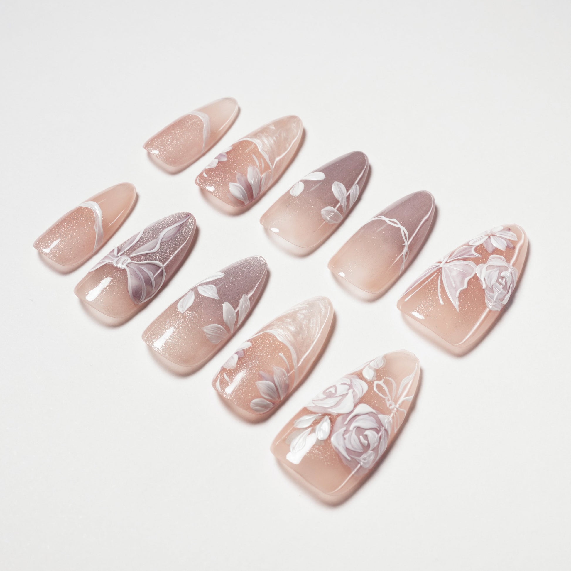 Set of pink and mauve artificial nails with white floral and bow designs on a white surface