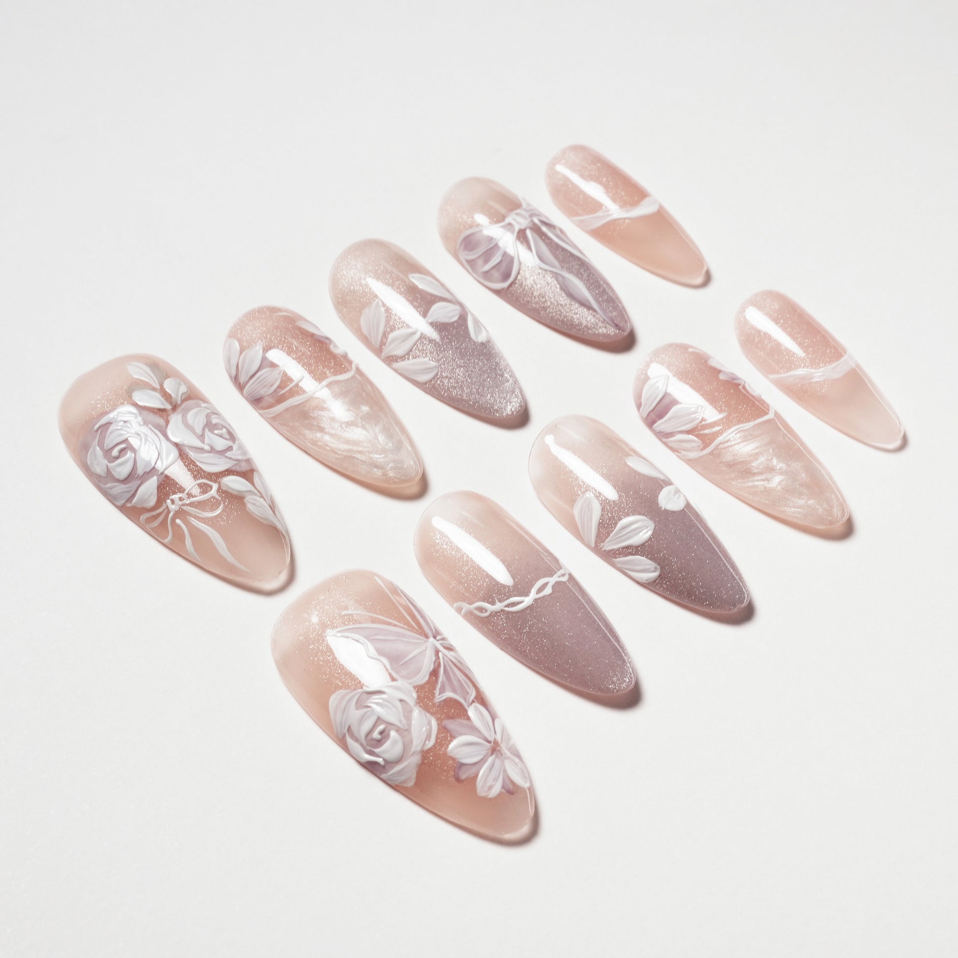 Set of nude and pink long press-on nails with white floral and leaf designs on white background