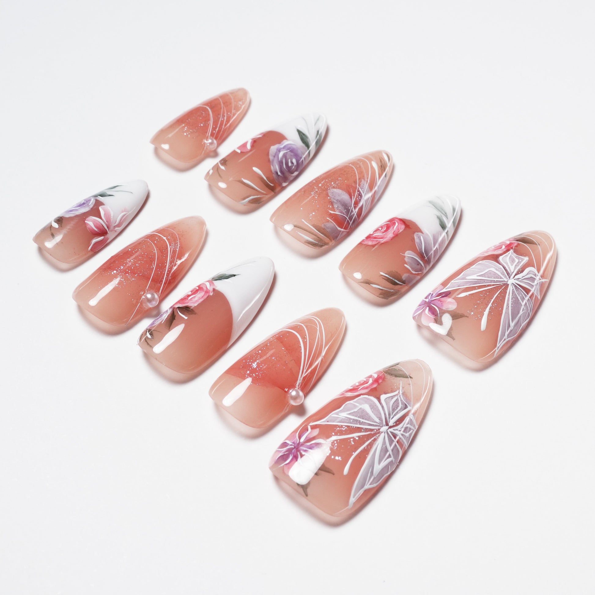 Handmade press-on nails with pink floral designs, white accents, pearls, and glossy finish