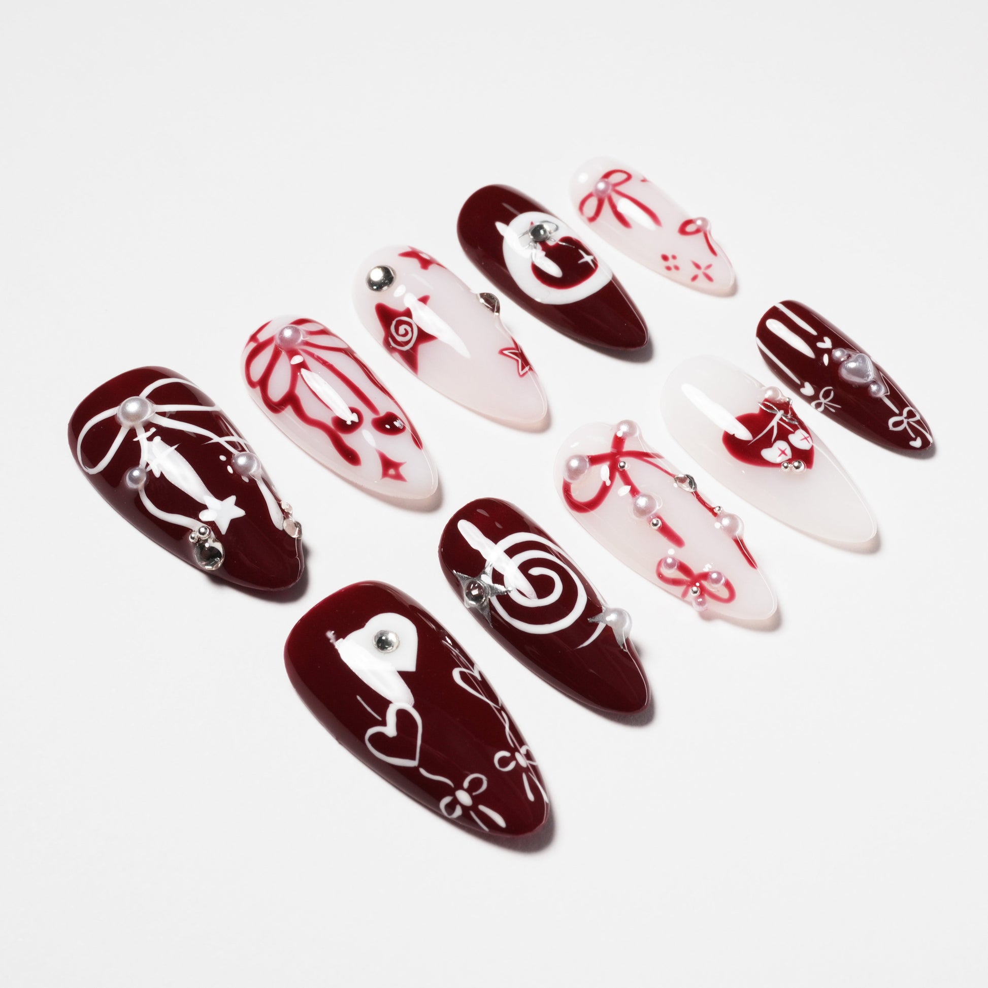 Handmade press-on nails in red and white with hearts, bows, pearls, and gemstone accents
