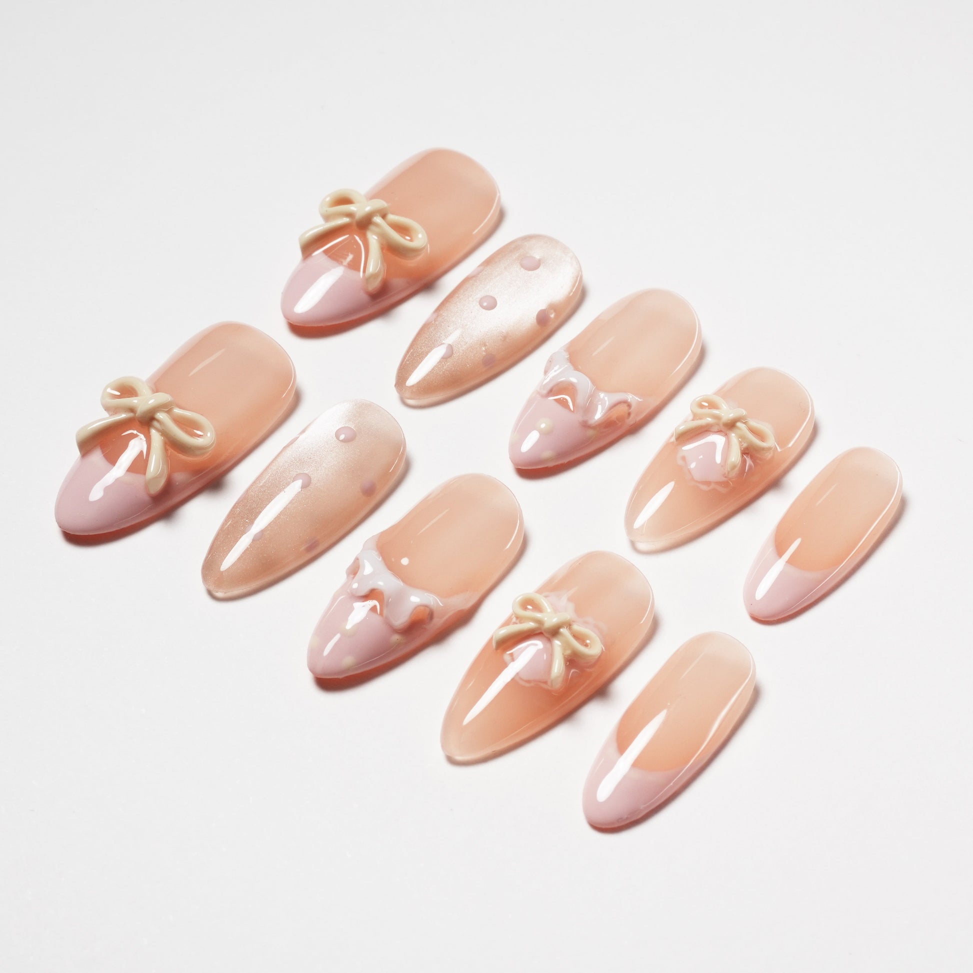 Set of nude and pink artificial nails with 3D bows, polka dots, and lace designs on white background