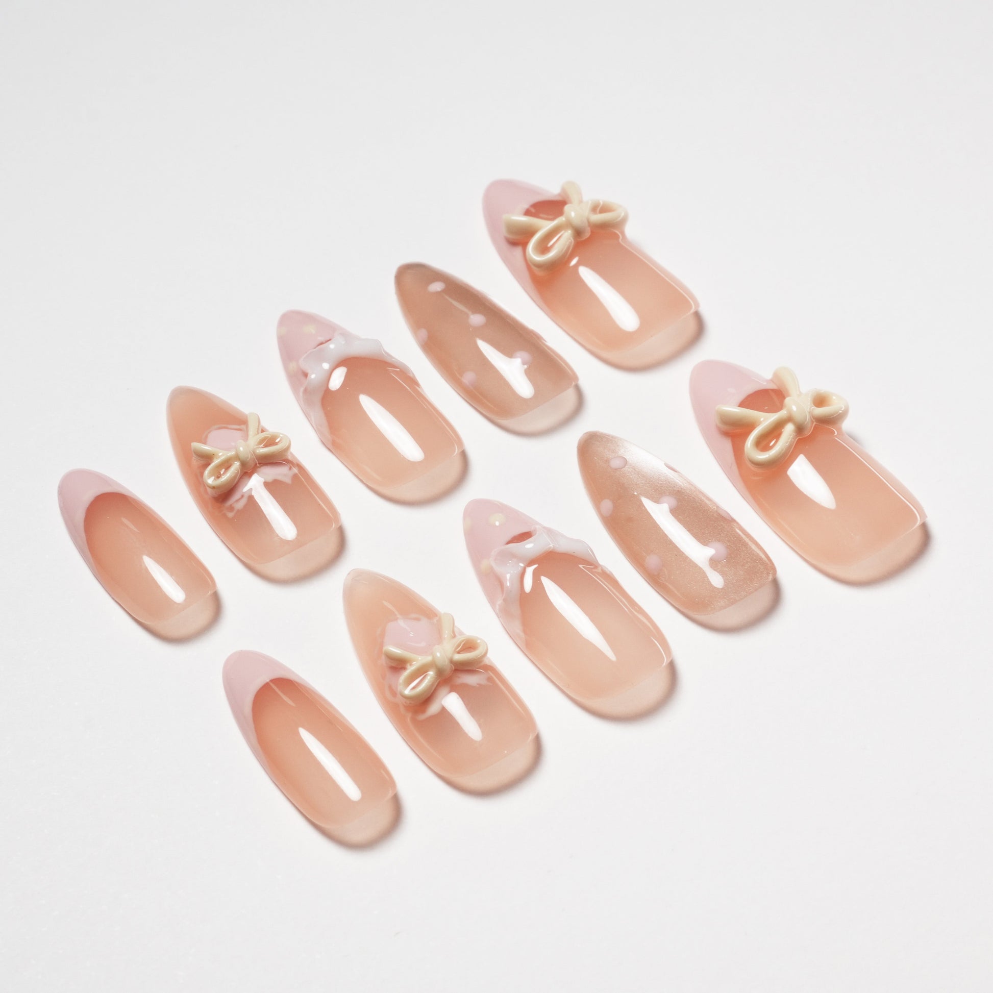 Set of nude and pink press-on almond-shaped nails with bows and polka dot accents