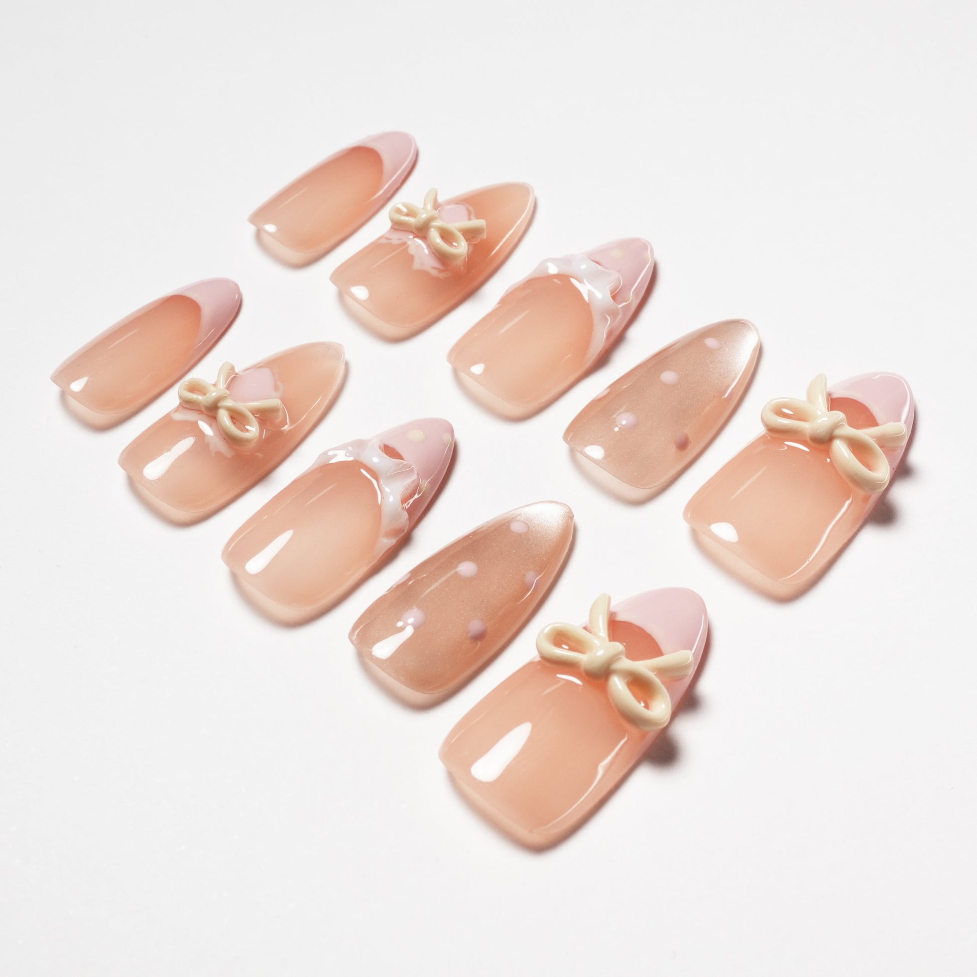 Set of glossy nude pink press-on nails with bows, polka dots, and glossy accents