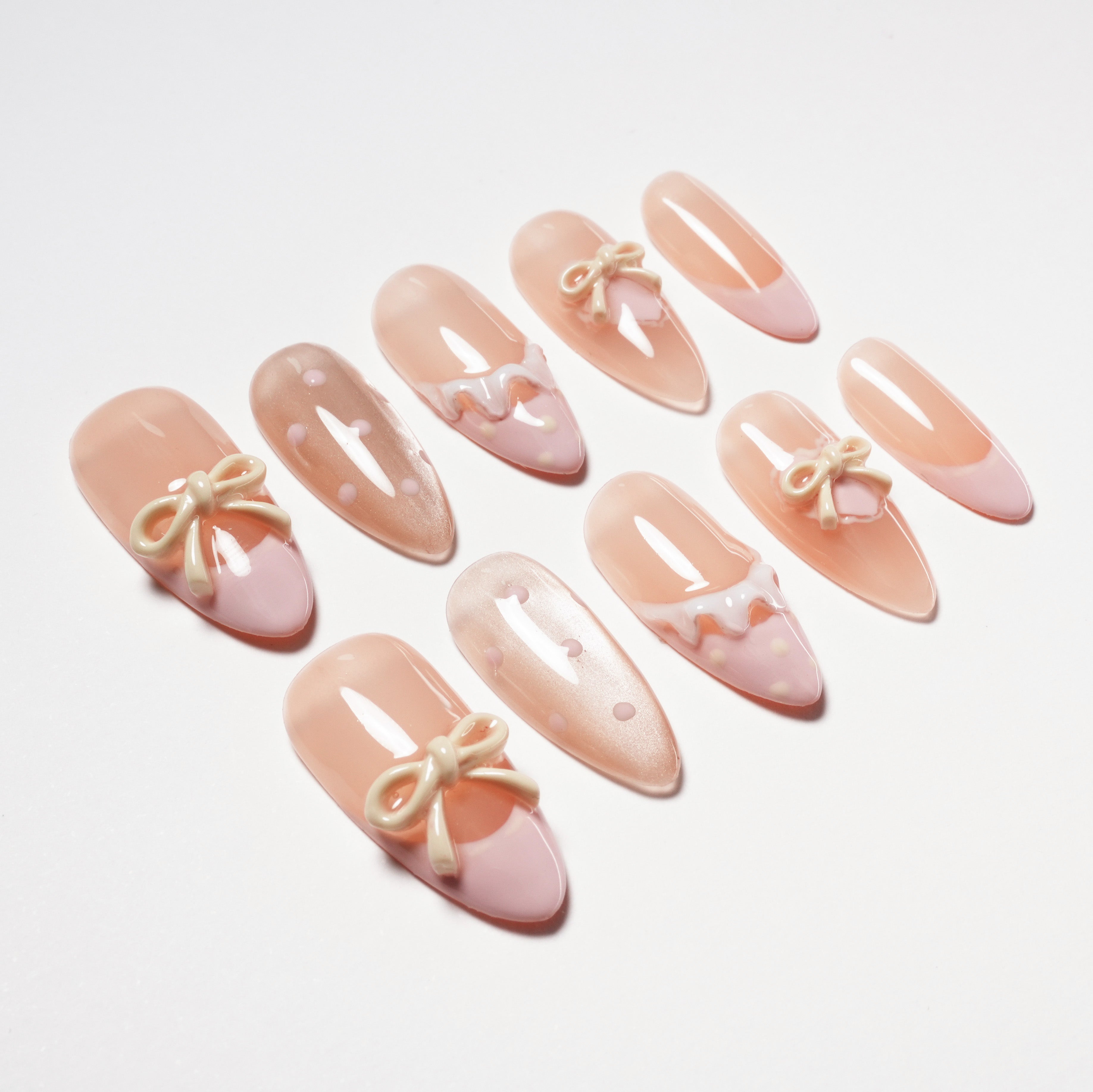 Set of pink and nude artificial nails with bow and polka dot nail art on white background
