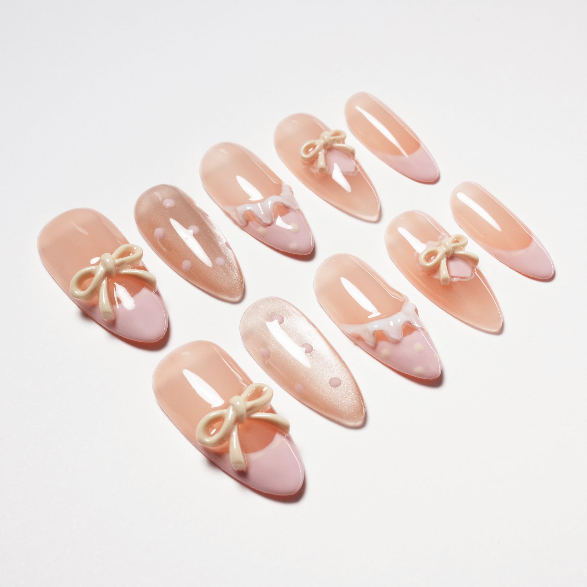 Set of pink and nude artificial nails with bow and polka dot nail art on white background