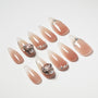 Glossy nude ombre press-on nails with rhinestone and gem accents on a white background