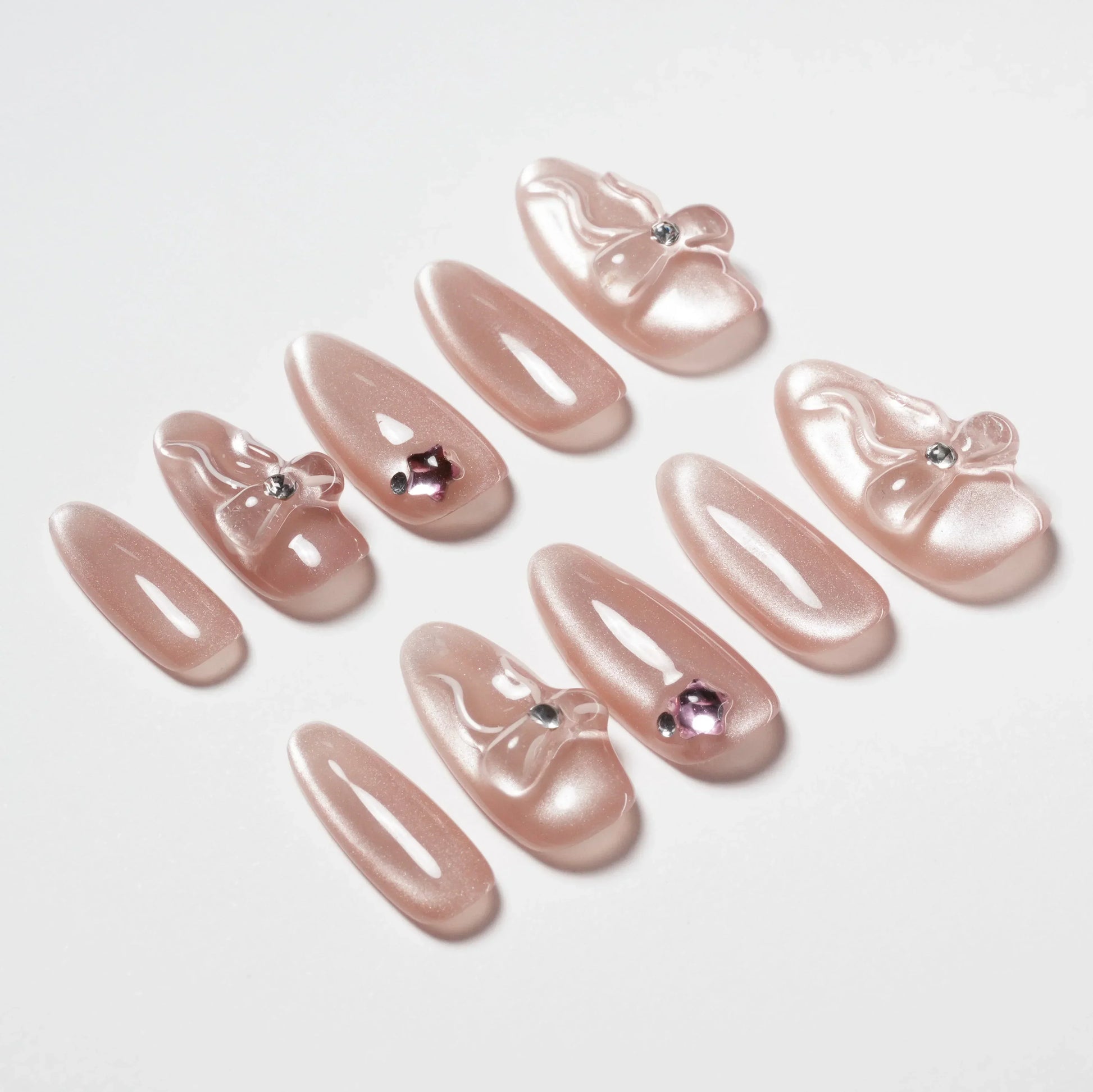 Set of pink pearlescent press-on nails with 3D bows and rhinestone accents on white background