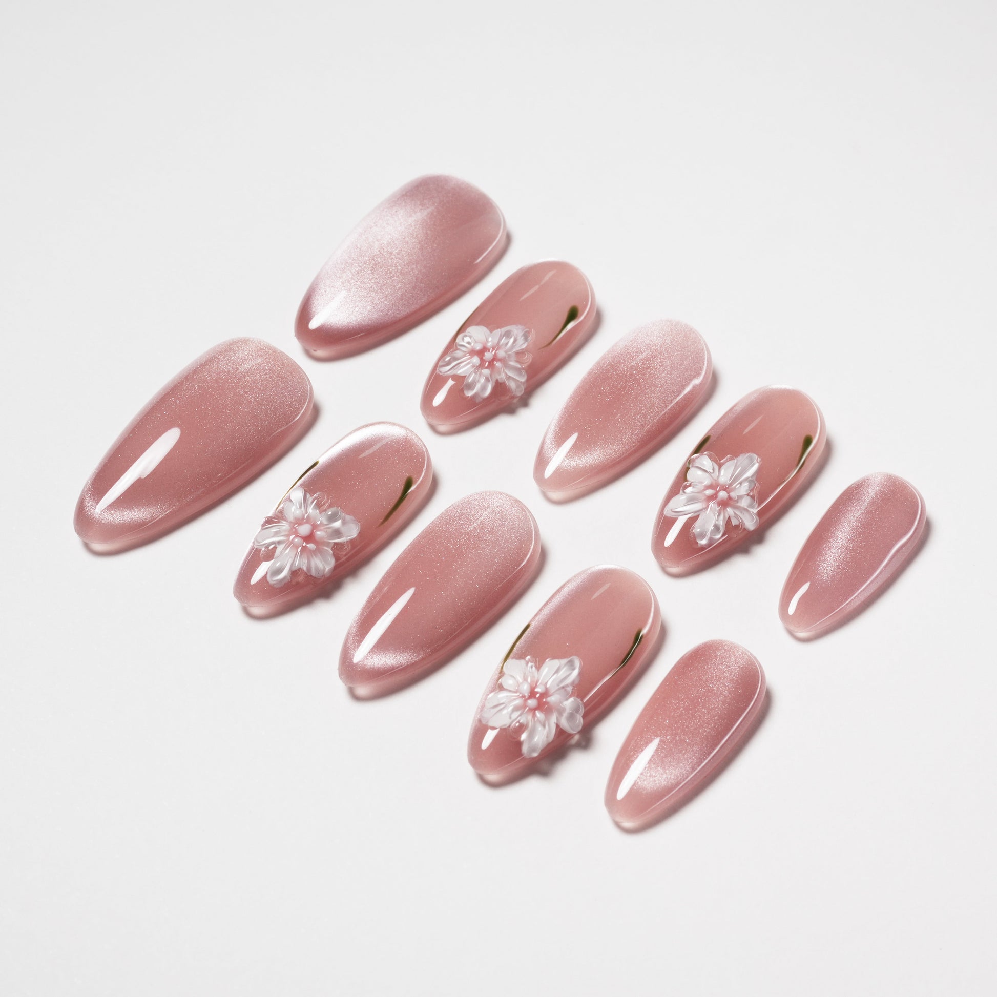 Handmade pink press-on nails with sparkly finish and 3D white floral accents, arranged on white
