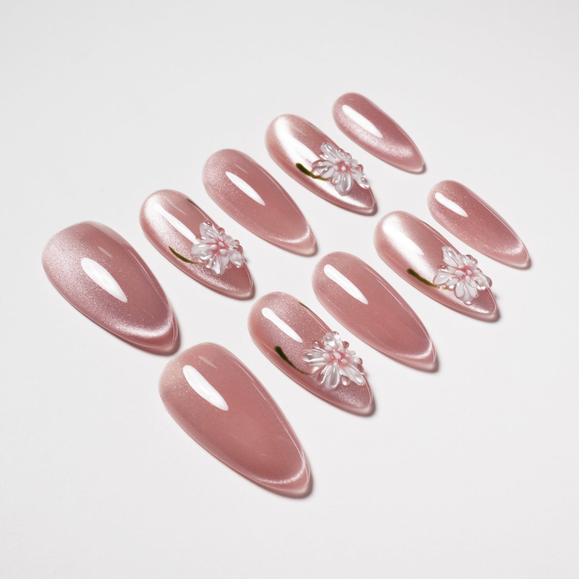 Glossy pink press-on nails with white 3D flower accents, almond shape, on white background.