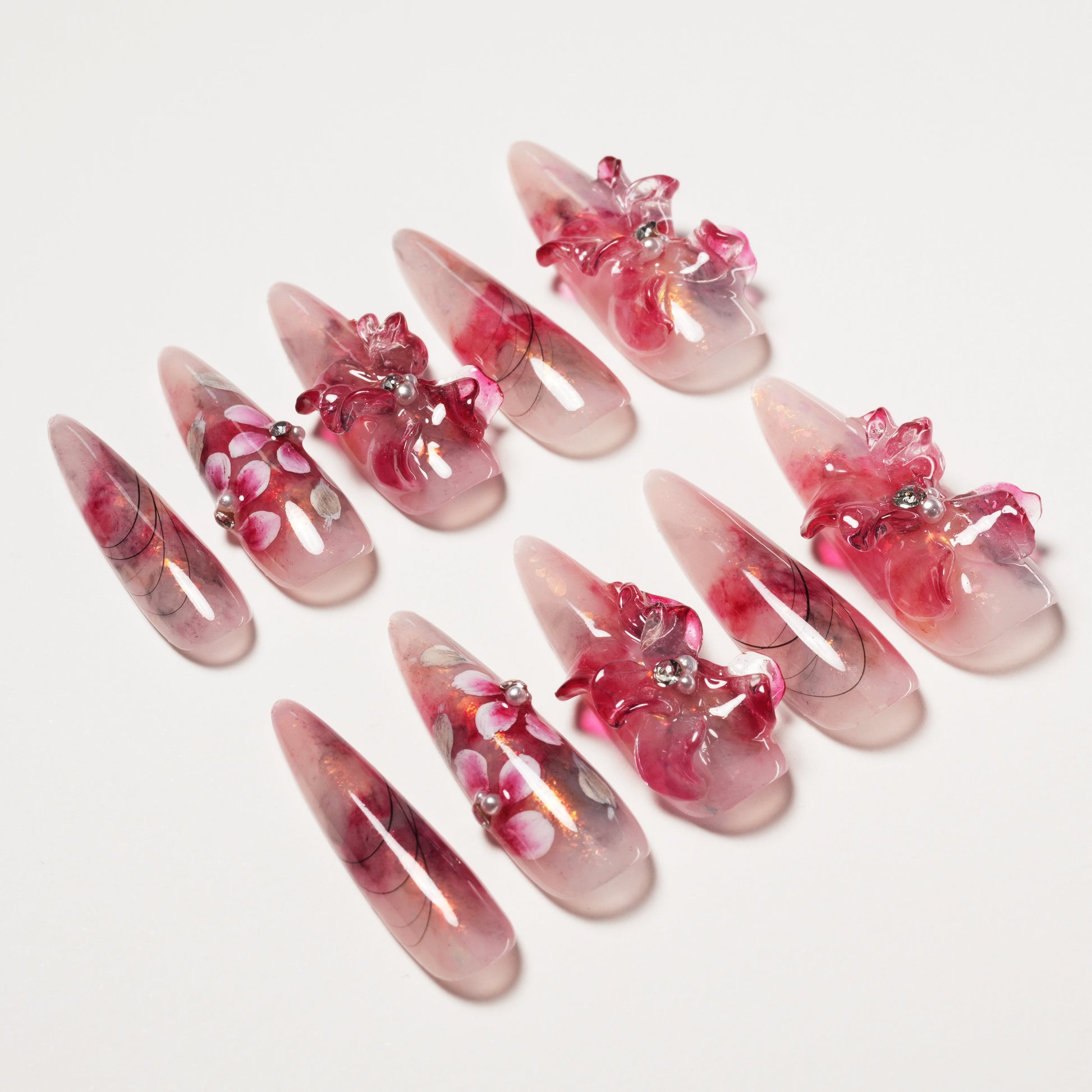 Set of long, pointed pink press-on nails with floral 3D and painted designs on white background