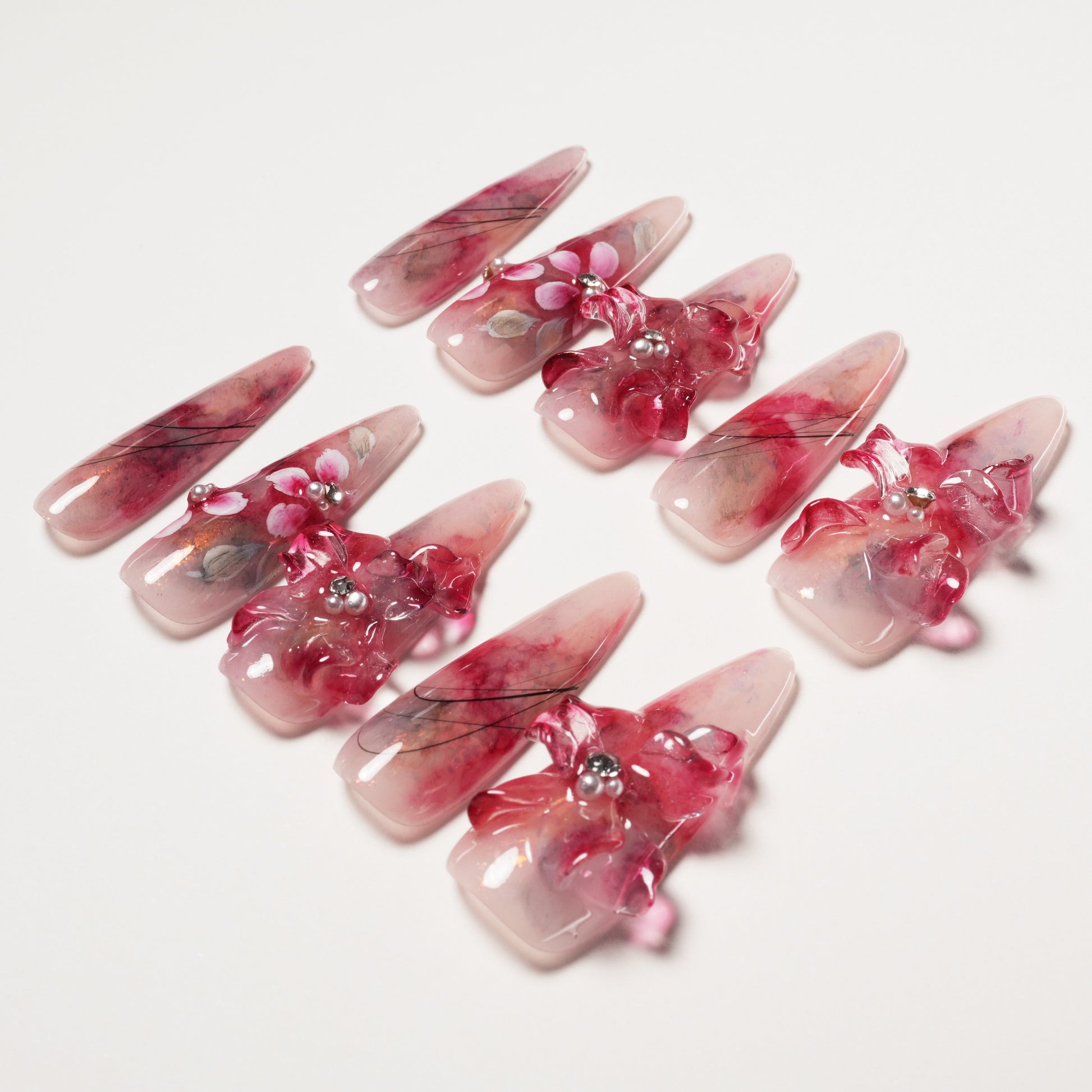 Set of long almond shaped pink resin nails with 3D flowers and pearl accents on white background