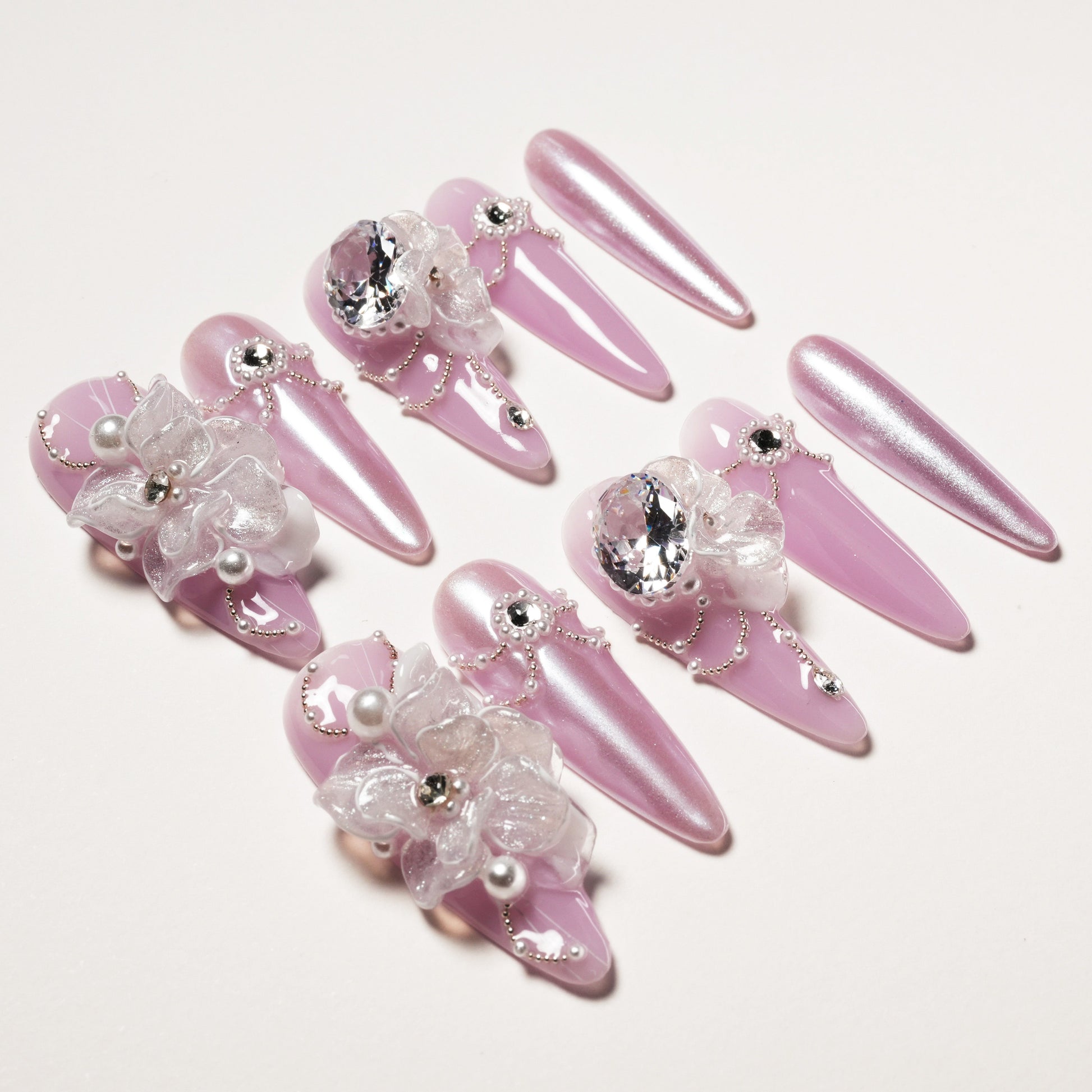 Set of pink glossy stiletto false nails adorned with 3D flowers, crystals, pearls, and silver bead chains