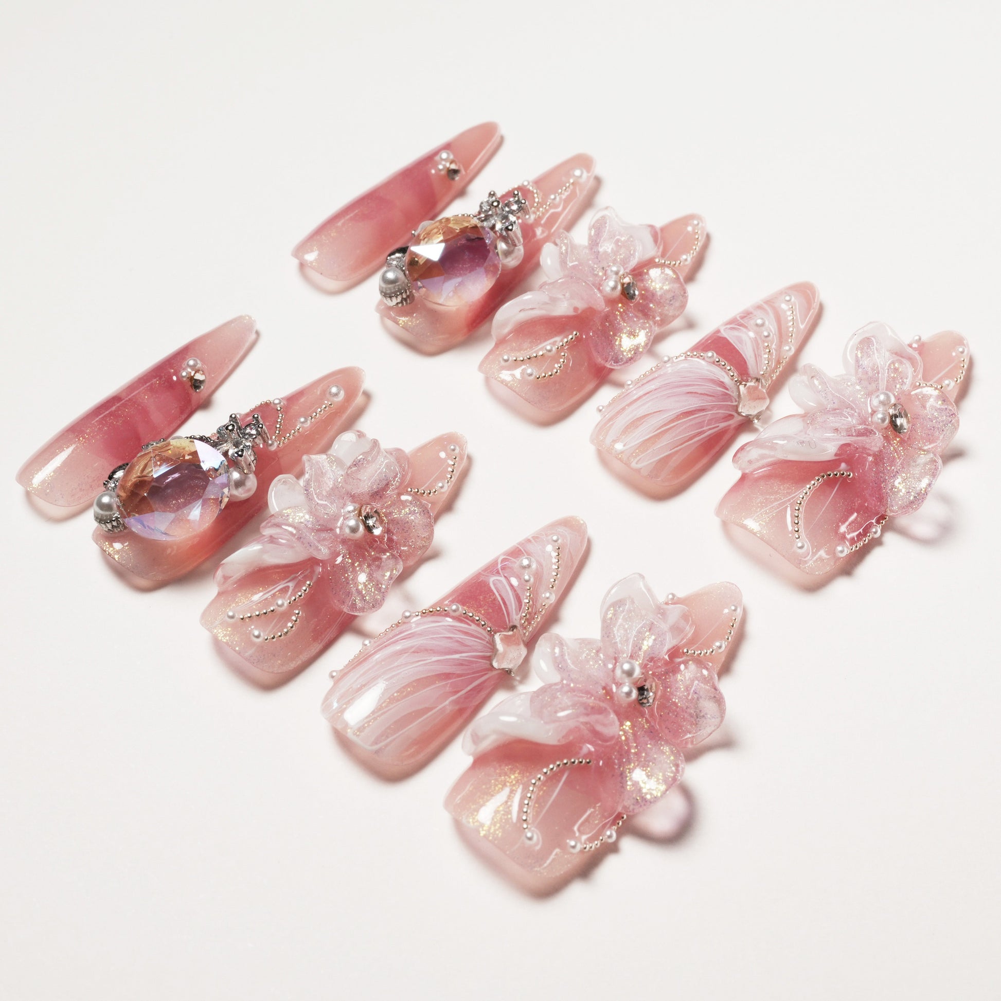 Elegant pink press-on nails with 3D flowers, rhinestones, pearls, and intricate silver bead designs