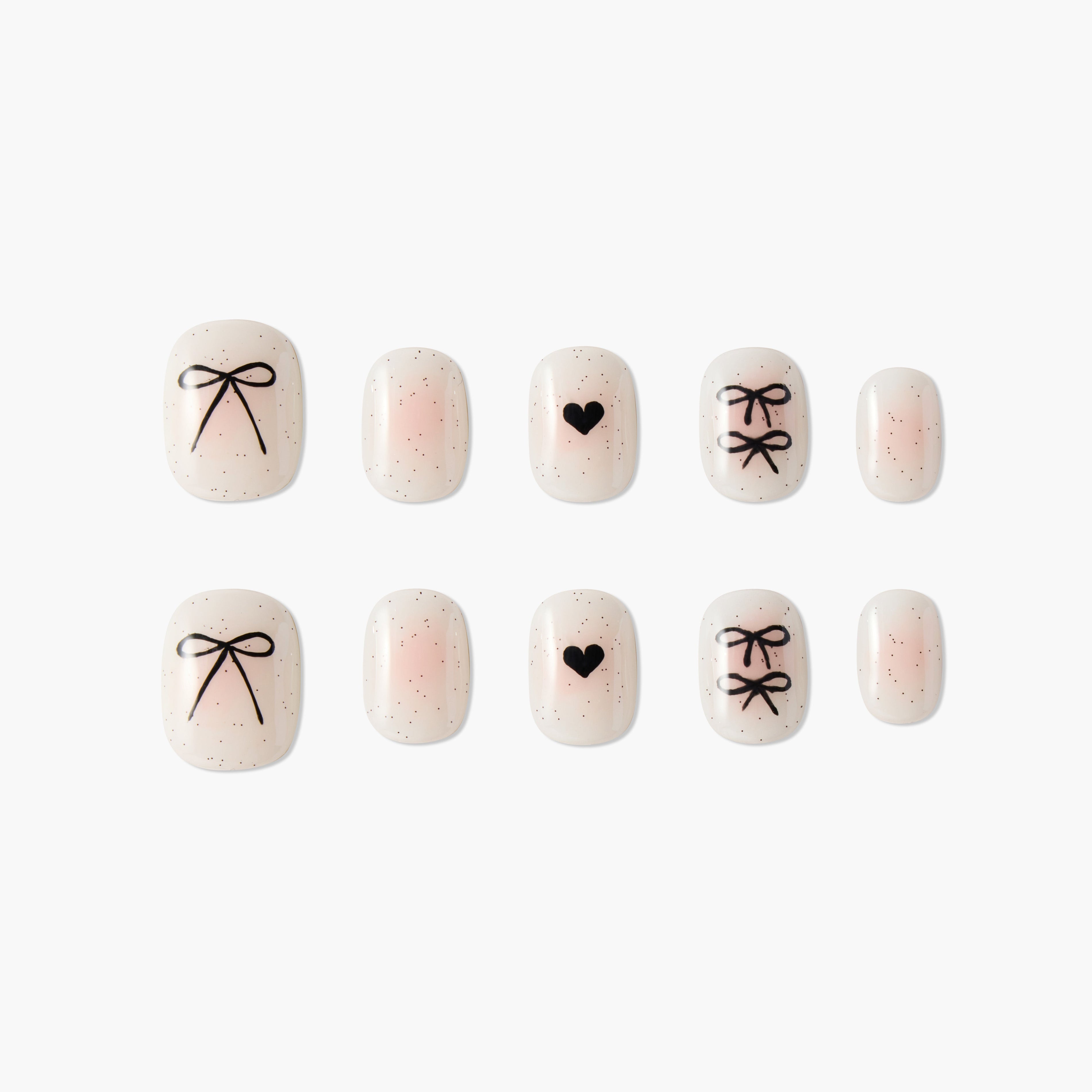 Set of beige false nails with black heart and bow designs and tiny black speckles