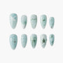 Light blue press-on nails with white bows, green accents, pearls, and star designs