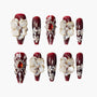 Set of red acrylic nails with white 3D flowers, gold accents, pearls, and rhinestone embellishments