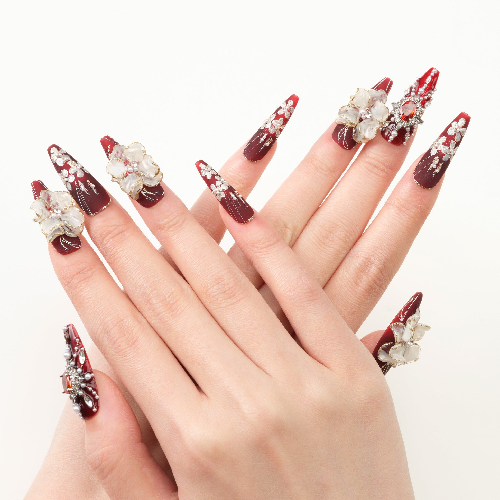 Hands with long red ombre nails decorated with white 3D flowers and rhinestones