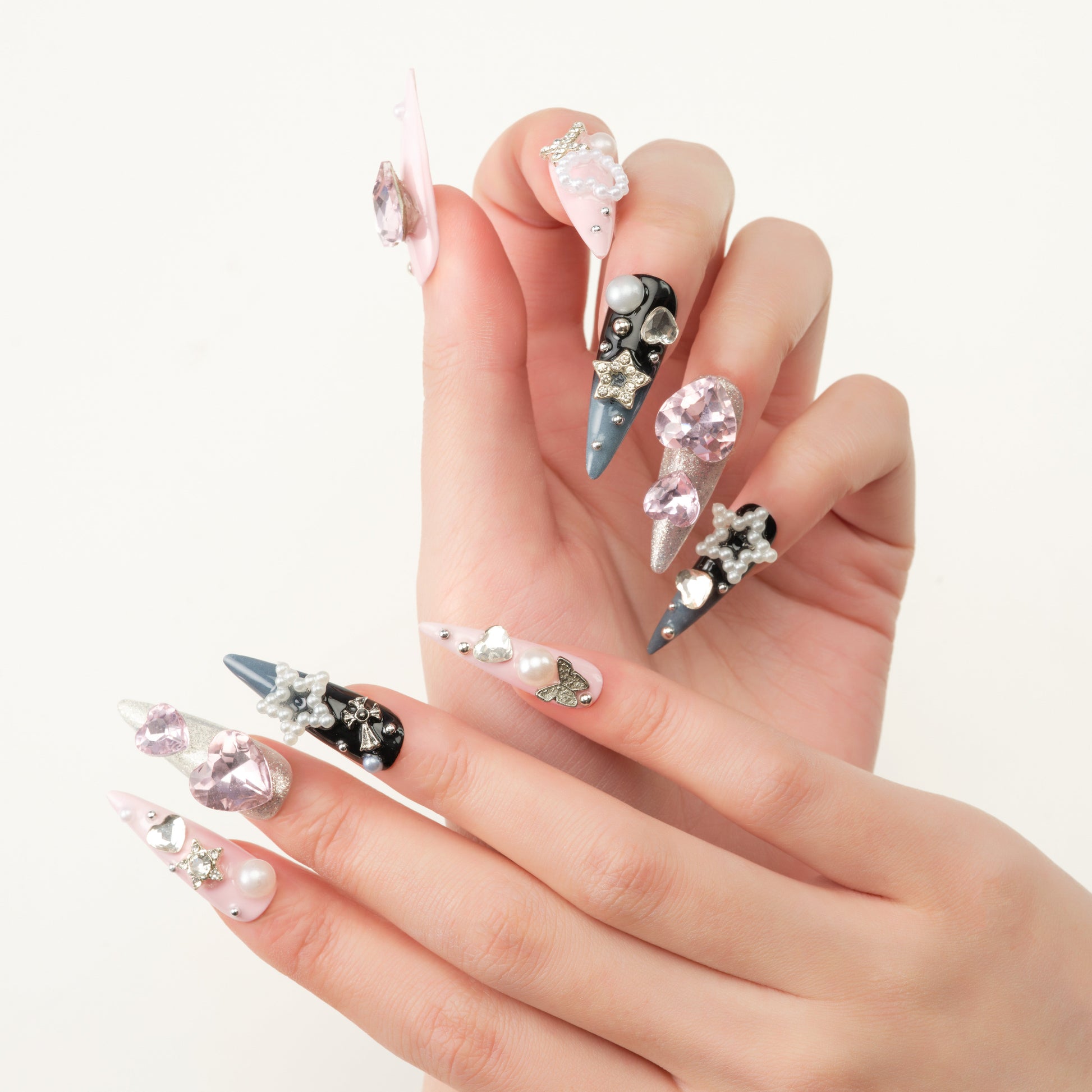 Stiletto-shaped nails with pink, black, and silver polish decorated with pearls, rhinestones, and heart gems