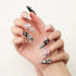 Close-up of hand with long stiletto nails featuring black, pink, and silver polish with jeweled and pearl decorations