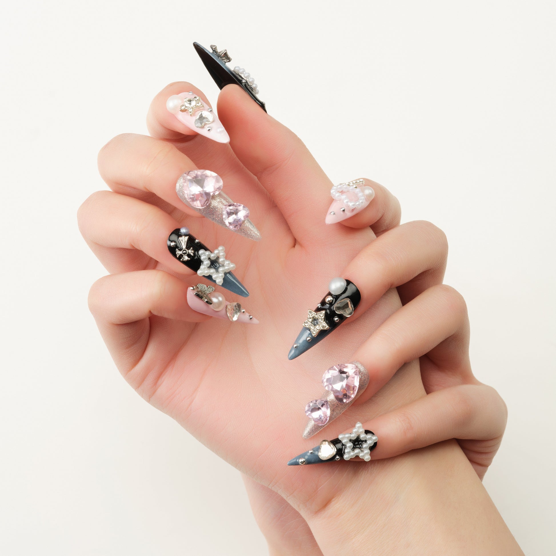 Close-up of hand with long stiletto nails featuring black, pink, and silver polish with jeweled and pearl decorations