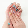 Hand with colorful handmade press-on nails featuring floral, gemstone, and abstract nail art designs