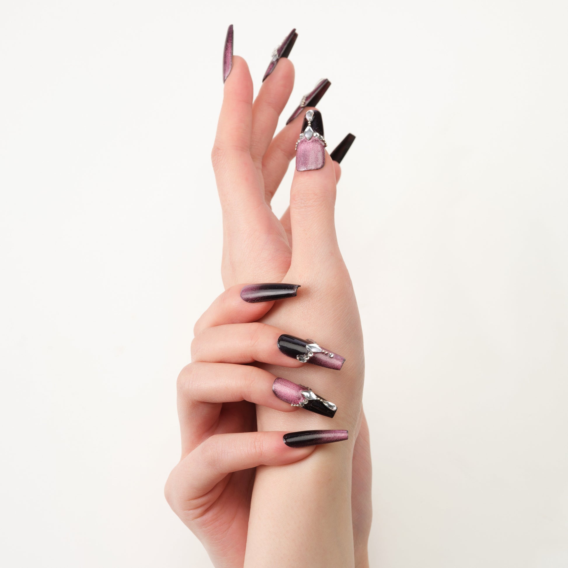 Long press-on nails with black and metallic mauve polish, rhinestone nail art, on model hand