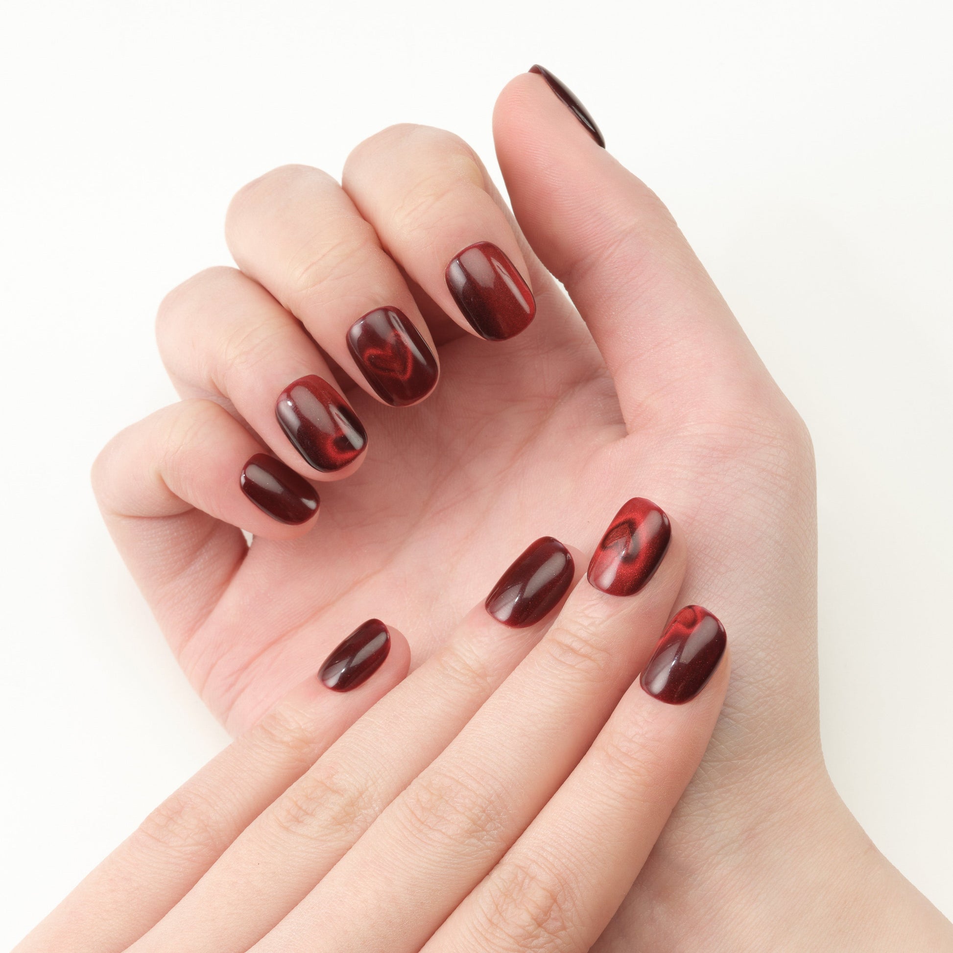 Hand with glossy deep red marble press-on nails on a light background