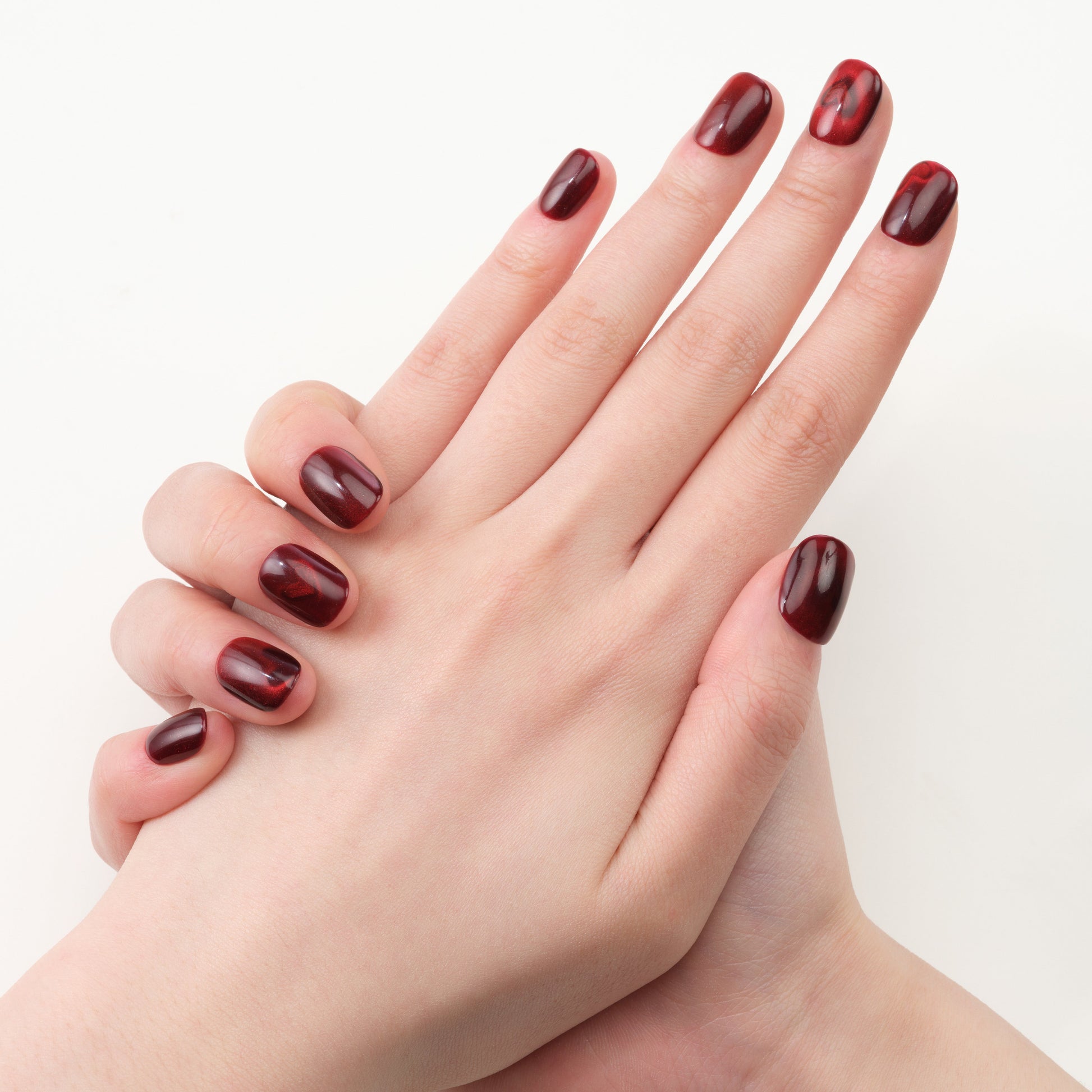 Hands with glossy deep red press-on nails featuring subtle marble accents on a white background.