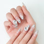 Hand with pointed silver French tip press-on nails, rhinestone and pearl nail art design